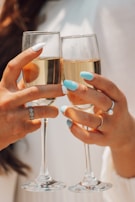 A close-up of a woman’s hand adorned with luxury rings holding a glass of champagne.