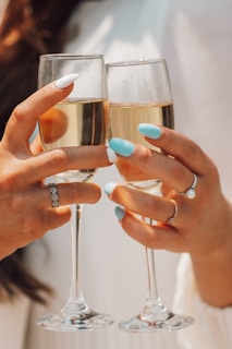 A close-up of a woman’s hand adorned with luxury rings holding a glass of champagne.