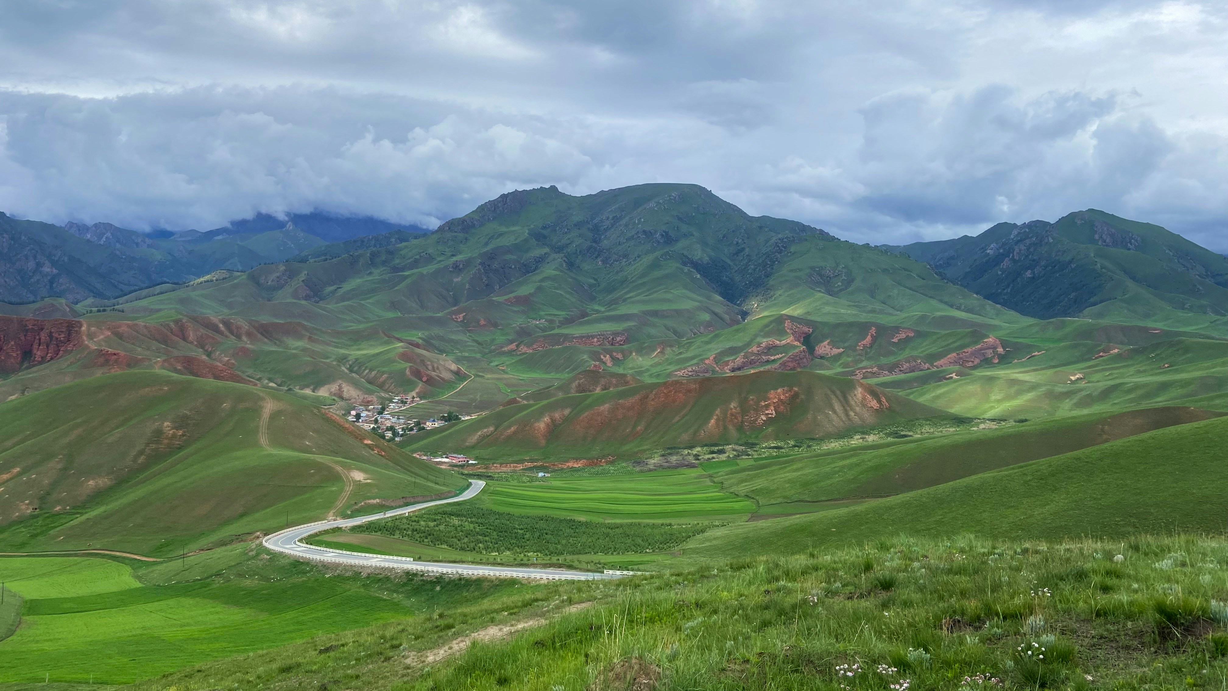 green grass field and mountains under white clouds and blue sky during daytime