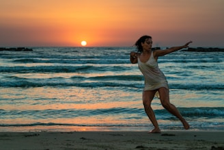 Full-screen video still showing women moving gracefully on the beach with sunlight highlighting fitness outfits in black, white, gold, ocean blue, and nude tones