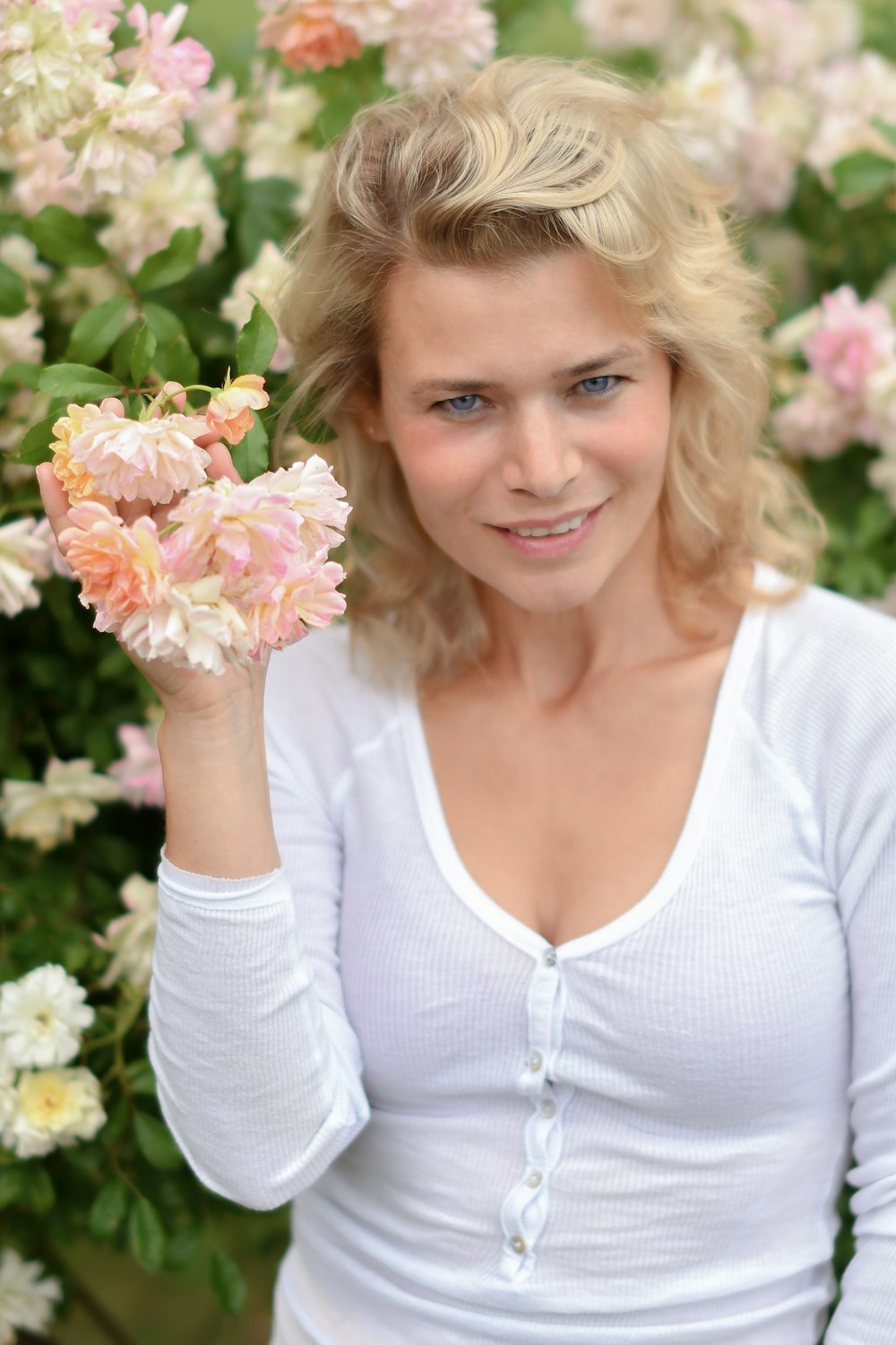 woman in white v neck long sleeve shirt holding pink flower
