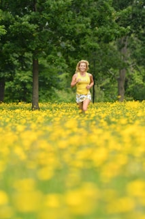 A person runs joyfully through a lush field filled with bright yellow flowers, surrounded by vibrant green trees.