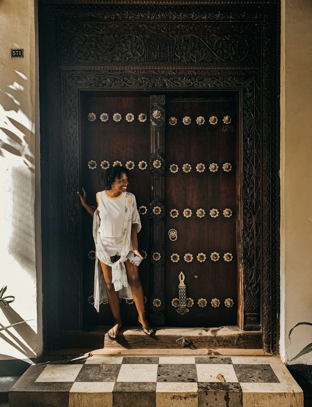 woman in white t-shirt and blue skirt standing in front of brown wooden door