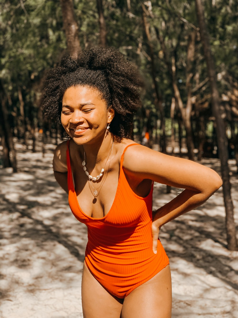 woman in orange tank top standing near trees during daytime