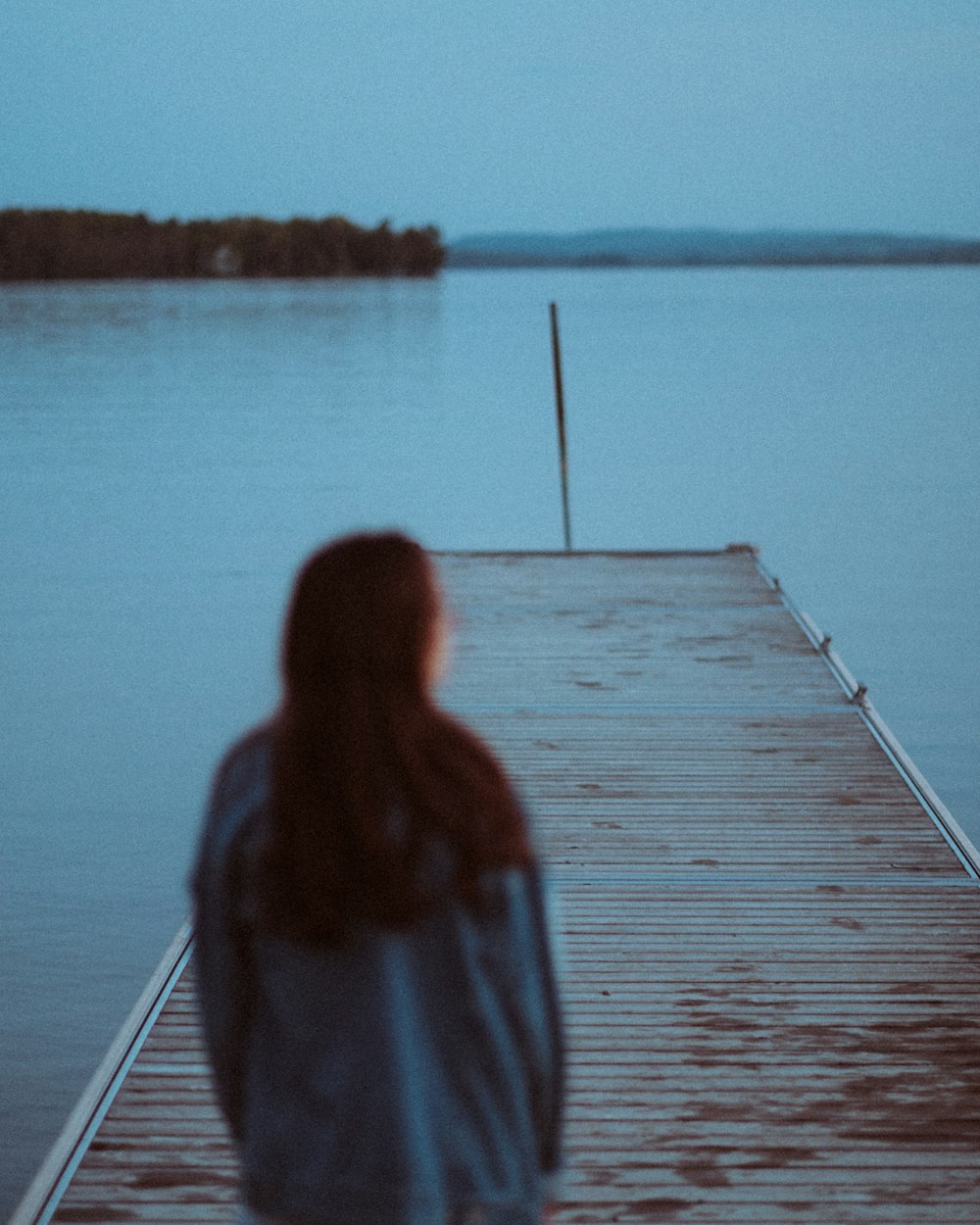 woman in gray jacket standing on wooden dock during daytime