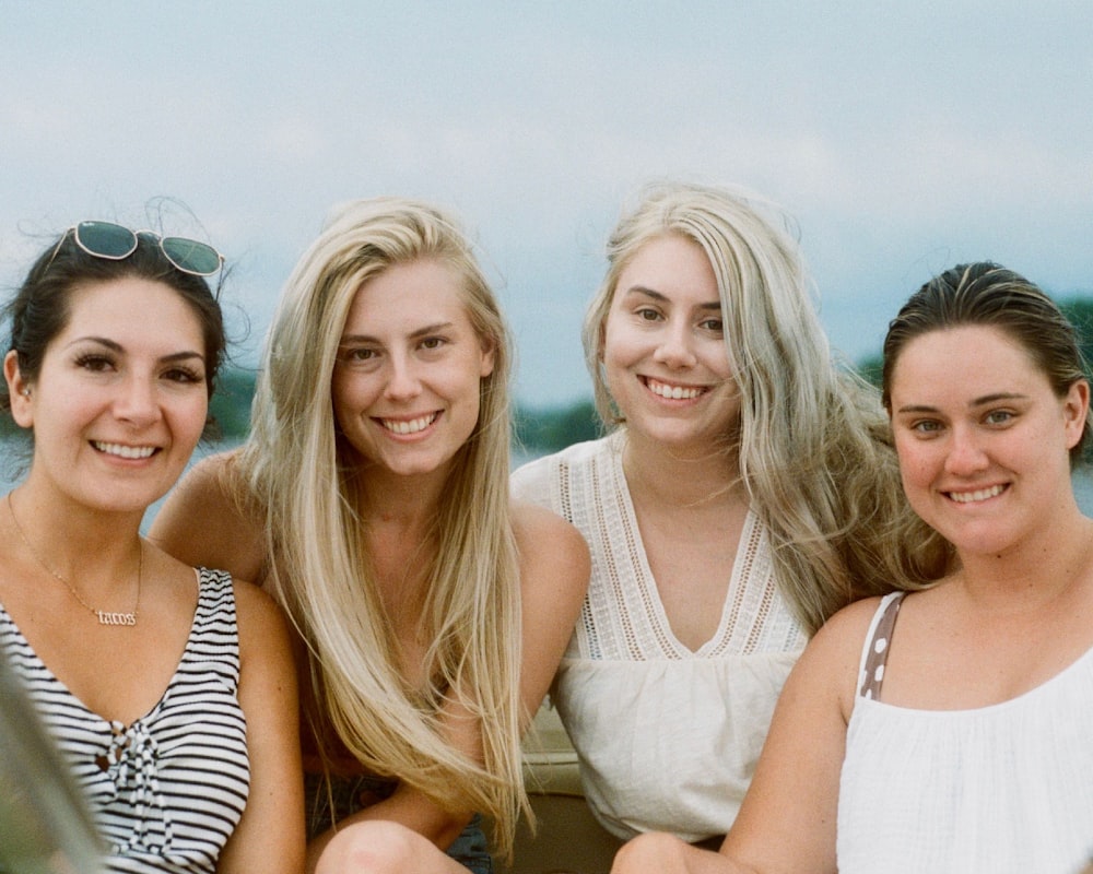 3 women smiling and sitting on brown wooden dock during daytime