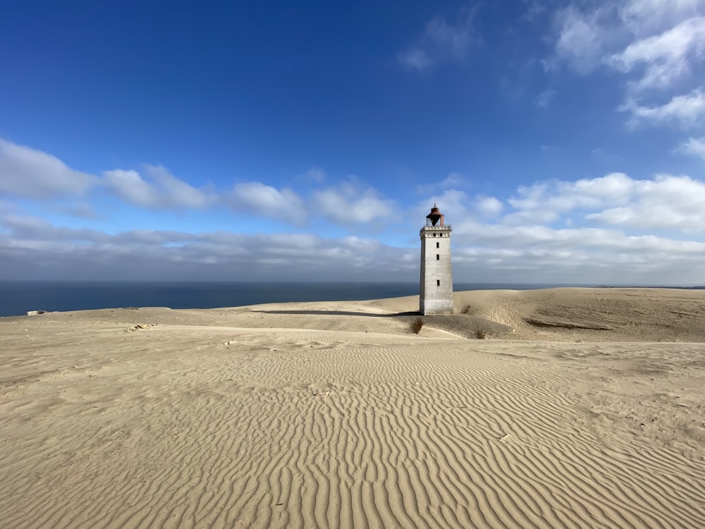 white lighthouse on brown sand under blue sky during daytime