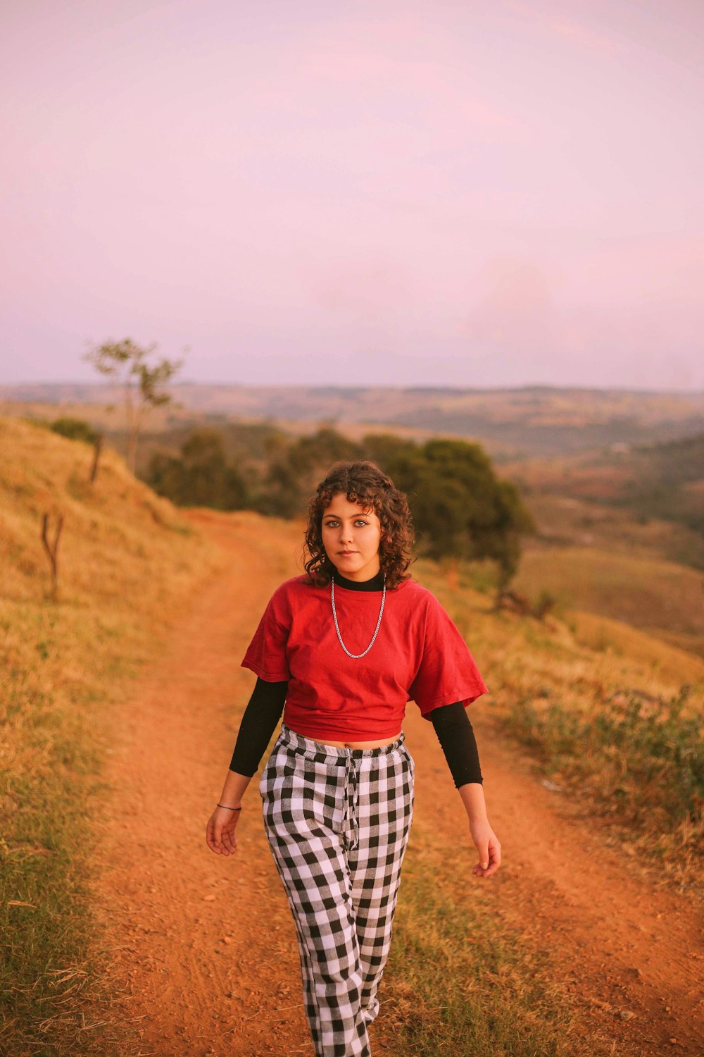 woman in red shirt and black and white checkered pants walking on brown field during daytime