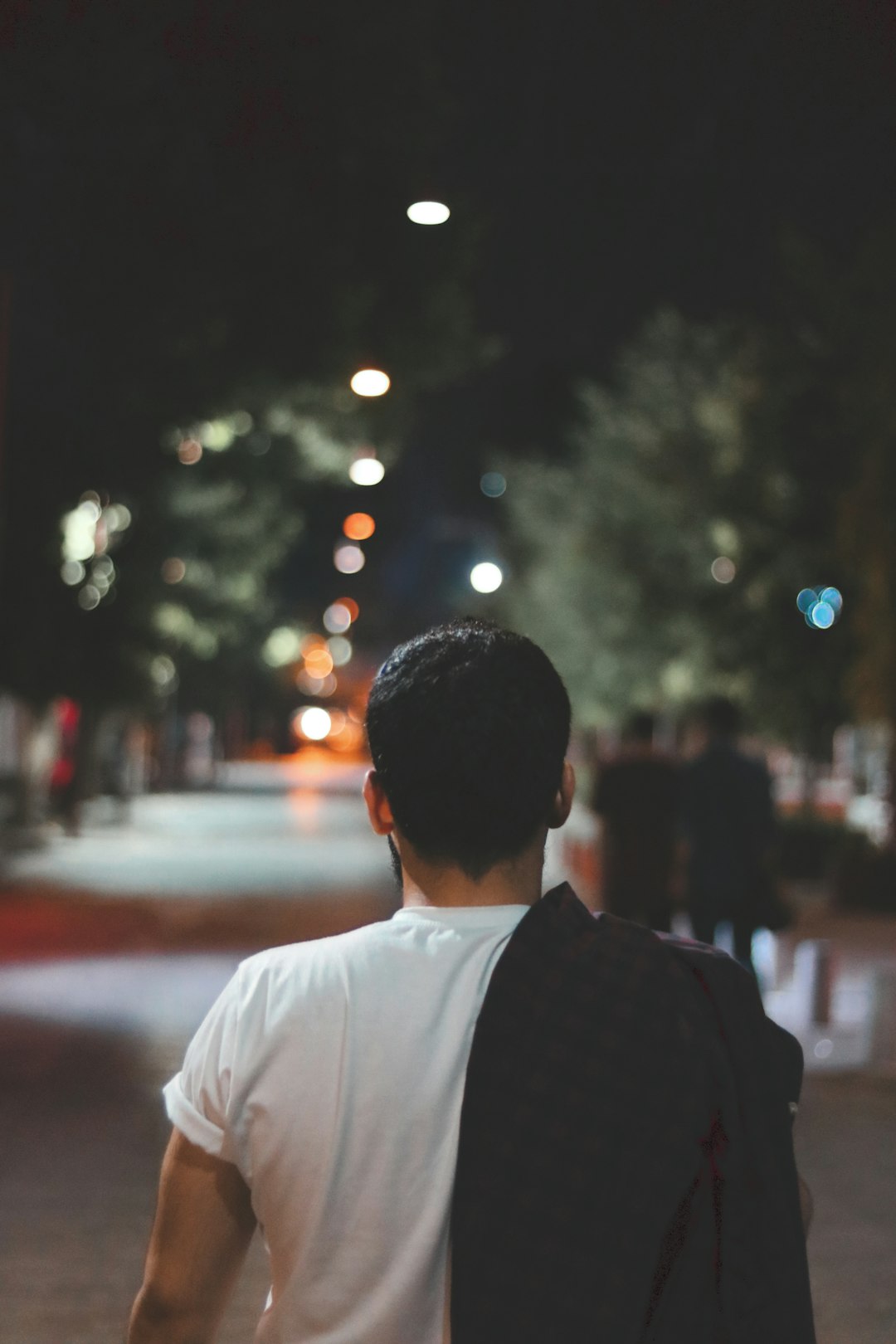 man in white dress shirt and black vest standing on sidewalk during night time