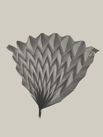 A detailed origami structure with multiple folds creating a symmetrical and fan-like pattern. The paper appears textured and is arranged in a visually appealing manner.