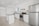 A modern kitchen featuring white cabinetry, stainless steel appliances, and a sleek black countertop. The room is well-lit with recessed lighting and has large floor tiles that add to the spacious feel. A small island provides additional workspace.