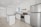 A modern kitchen featuring white cabinetry, stainless steel appliances, and a sleek black countertop. The room is well-lit with recessed lighting and has large floor tiles that add to the spacious feel. A small island provides additional workspace.