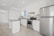 A modern kitchen featuring white cabinetry, stainless steel appliances, and a sleek black countertop. The room is well-lit with recessed lighting and has large floor tiles that add to the spacious feel. A small island provides additional workspace.