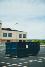 blue trash bin beside brown concrete building during daytime