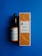 A bottle and a box of Éclat Natural Skincare Vitamin C Serum are placed against a solid blue background. The bottle has a black dropper cap, and the label matches the design on the box, which features an orange pattern with text indicating it is an anti-aging antioxidant product.