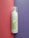 A bottle of aloe vera facial cleansing foam placed vertically against a split background of pink and purple. The bottle has a transparent cap and green aloe vera leaf graphics on its white surface.