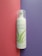 A bottle of aloe vera facial cleansing foam placed vertically against a split background of pink and purple. The bottle has a transparent cap and green aloe vera leaf graphics on its white surface.