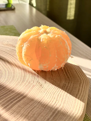 A peeler resting on a wooden table next to freshly peeled fruit, bathed in warm light.