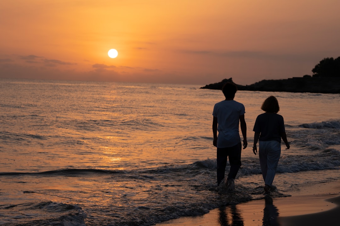 silhouette of 3 people standing on seashore during sunset