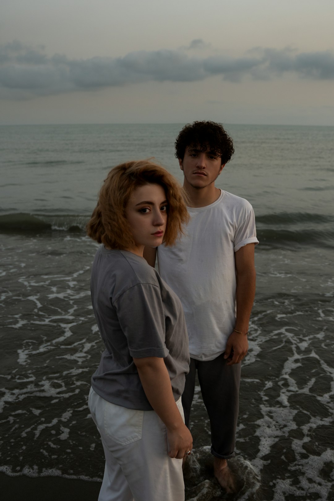 man in white crew neck t-shirt standing beside woman in gray t-shirt on beach