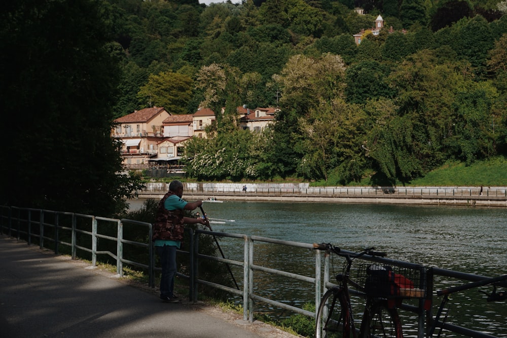 Mujer con chaqueta azul y pantalones negros de pie en el puente cerca del cuerpo de agua durante el día