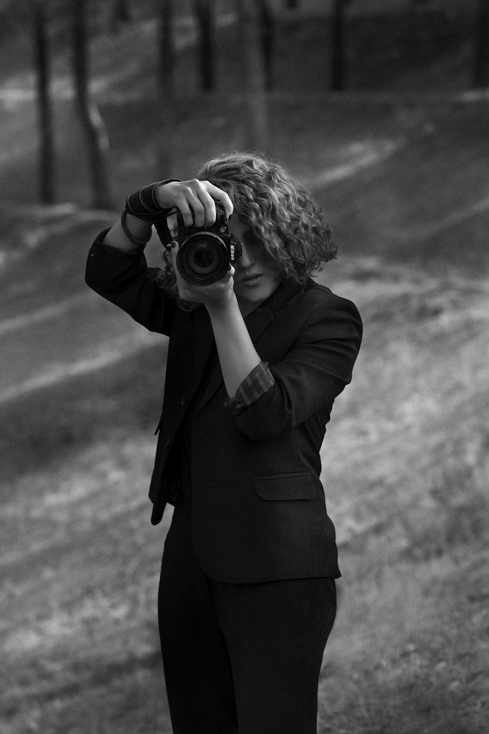 grayscale photo of woman in black coat holding camera