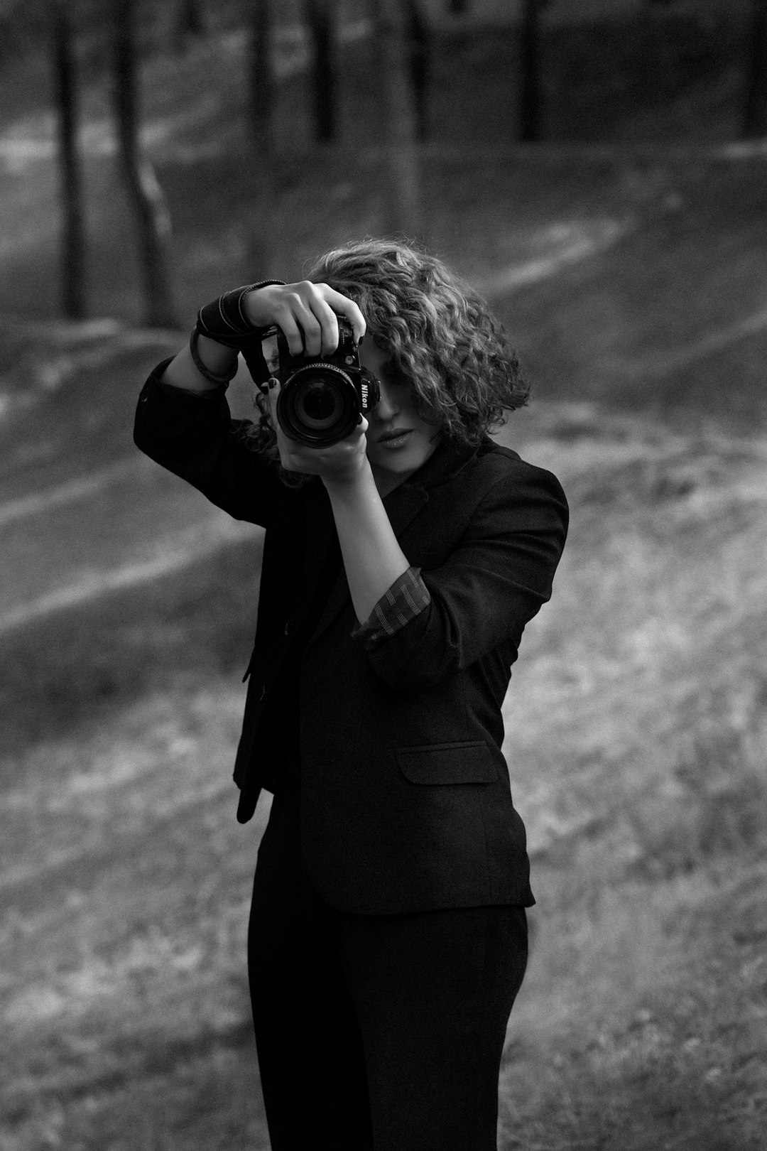 grayscale photo of woman in black coat holding camera