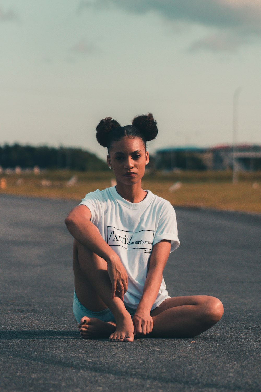 man in white crew neck t-shirt and blue shorts sitting on gray concrete road during