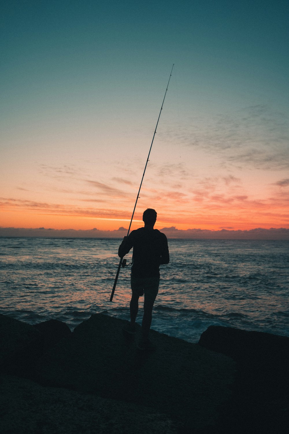 silhouette of man fishing on sea during sunset