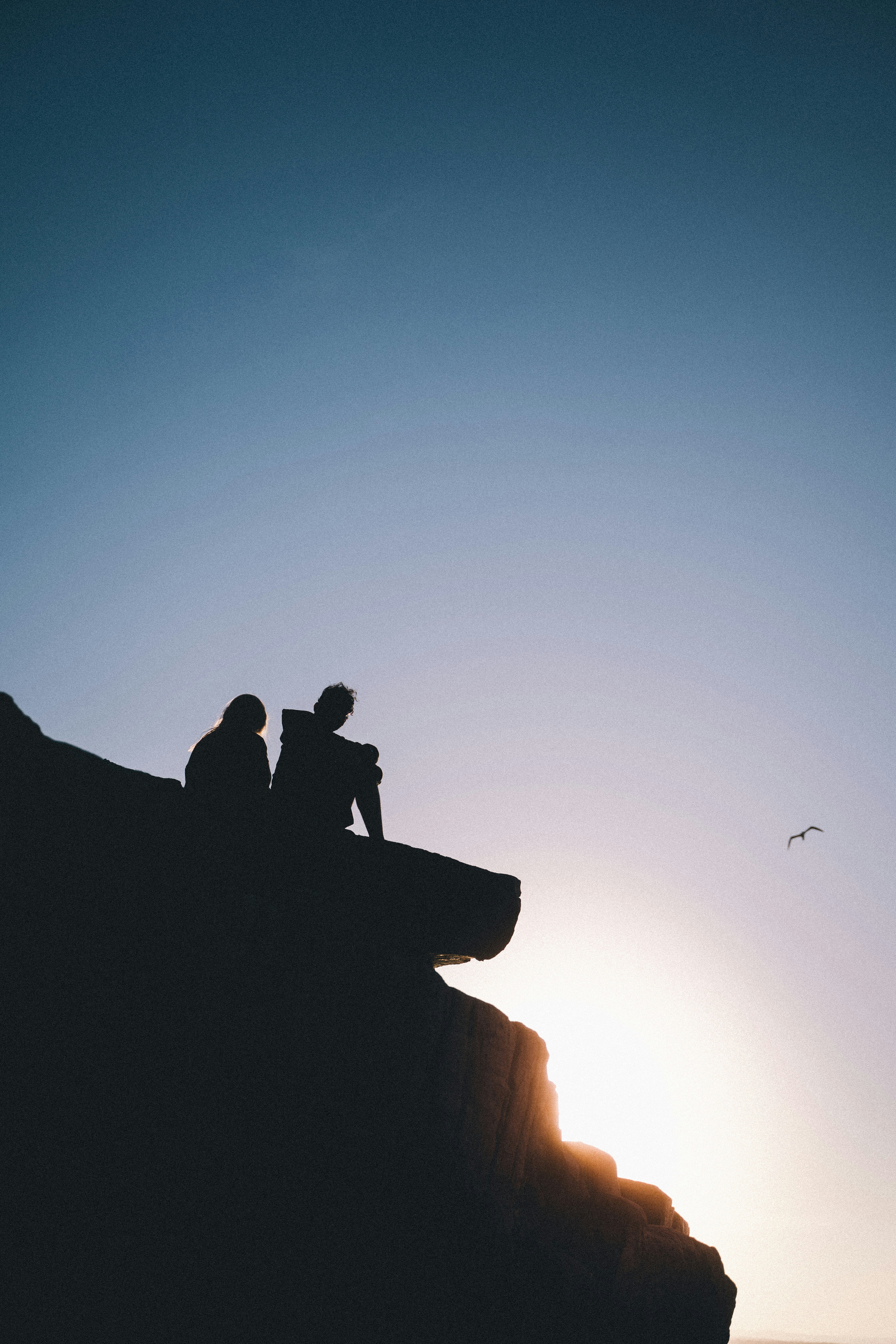 silhouette of 2 men sitting on rock formation during sunset