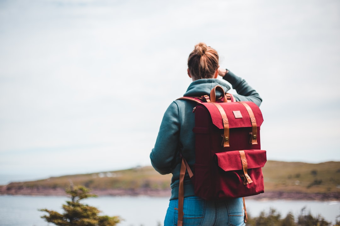 woman in blue denim jacket carrying red and black backpack