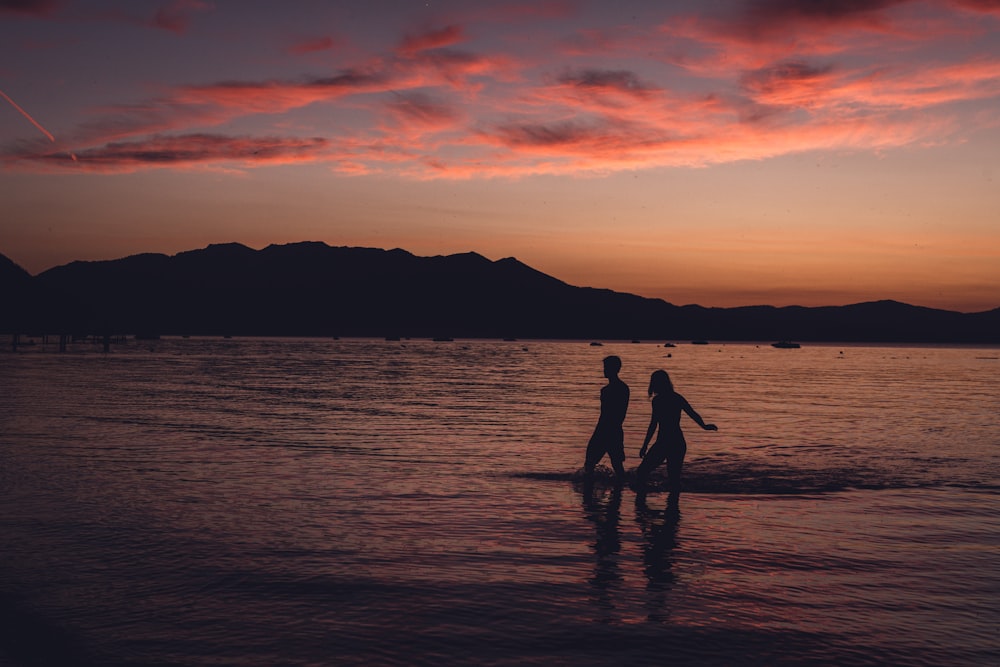 silhouette of 2 person standing on seashore during sunset