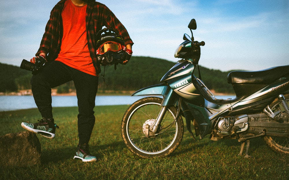 man in red jacket and black pants standing beside motorcycle during daytime