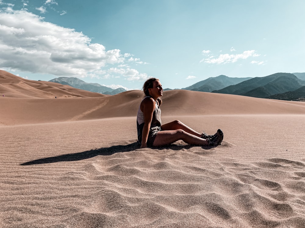 woman in white tank top and red pants sitting on brown sand during daytime