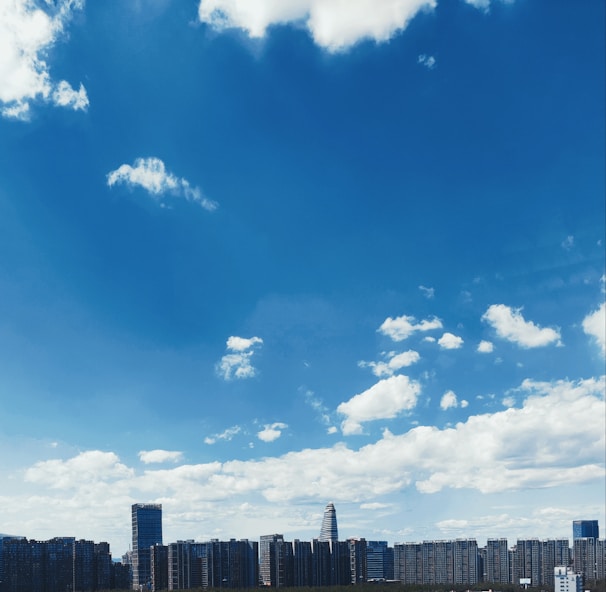 Crisp drone shot of a modern city skyline framed by a clear blue sky with soft clouds.