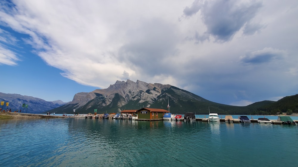 brown wooden house on body of water near mountain under white clouds during daytime