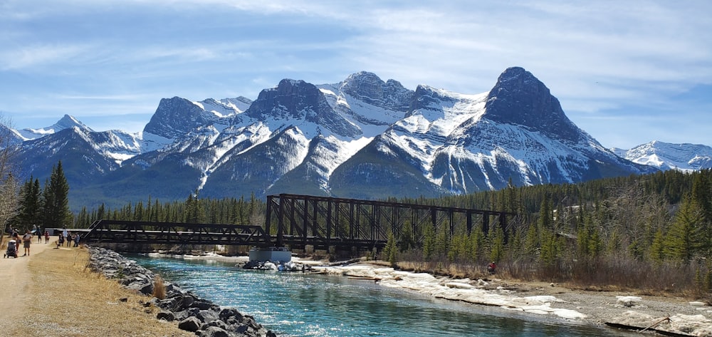 brown wooden bridge over river near snow covered mountain