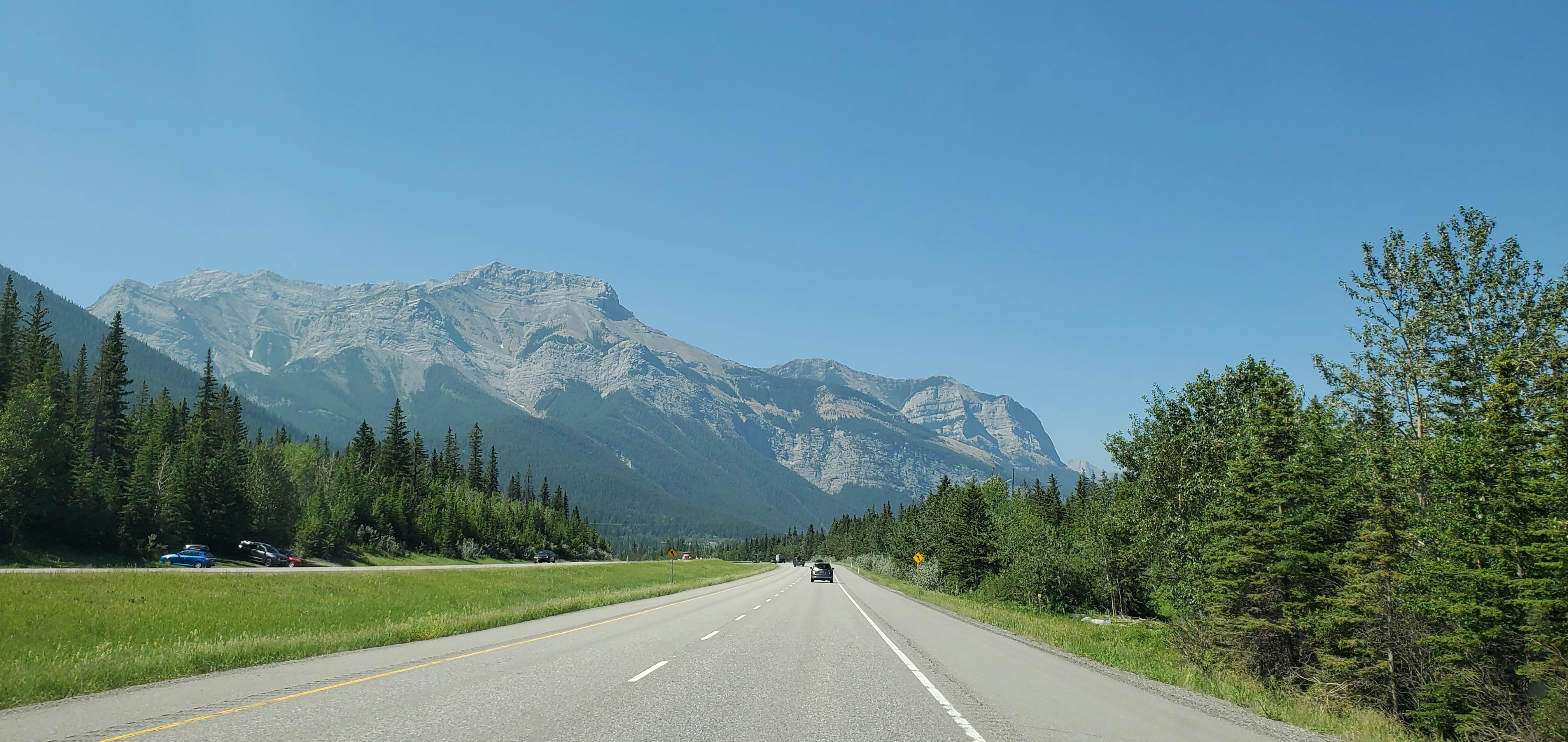 gray concrete road near green trees and mountain during daytime