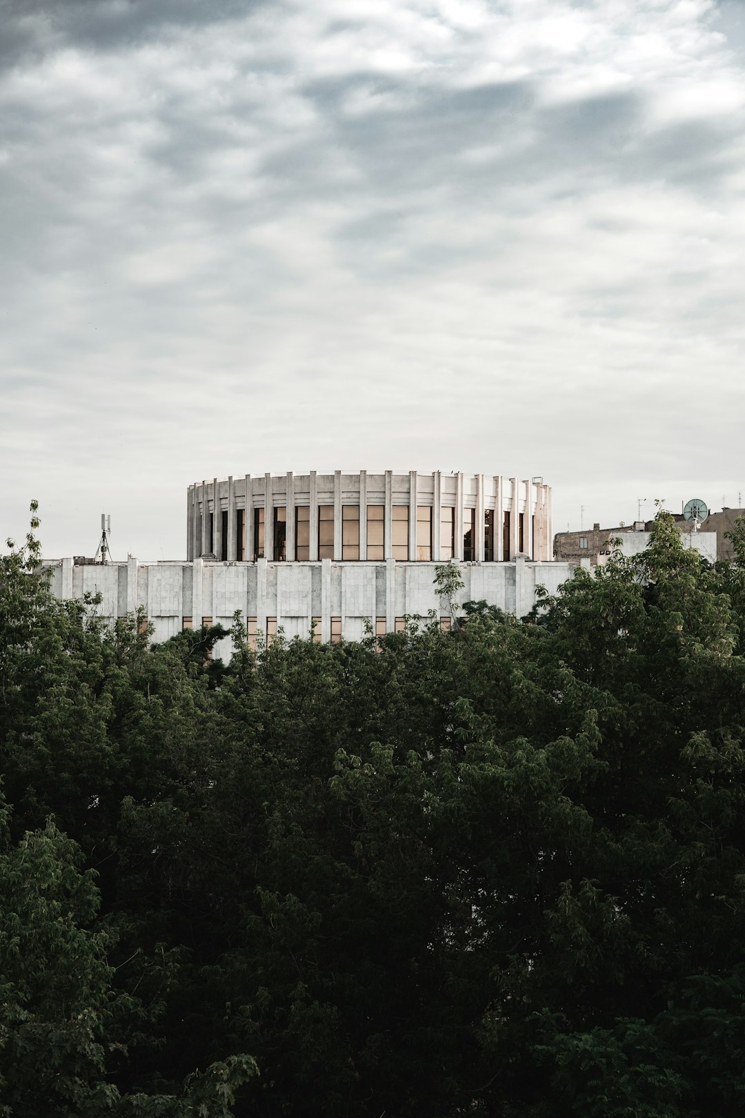 white concrete building near green trees under white clouds during daytime