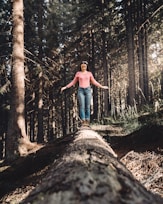 woman in blue denim jeans standing on brown tree log during daytime