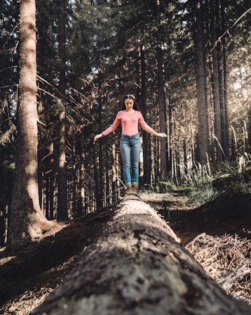woman in blue denim jeans standing on brown tree log during daytime