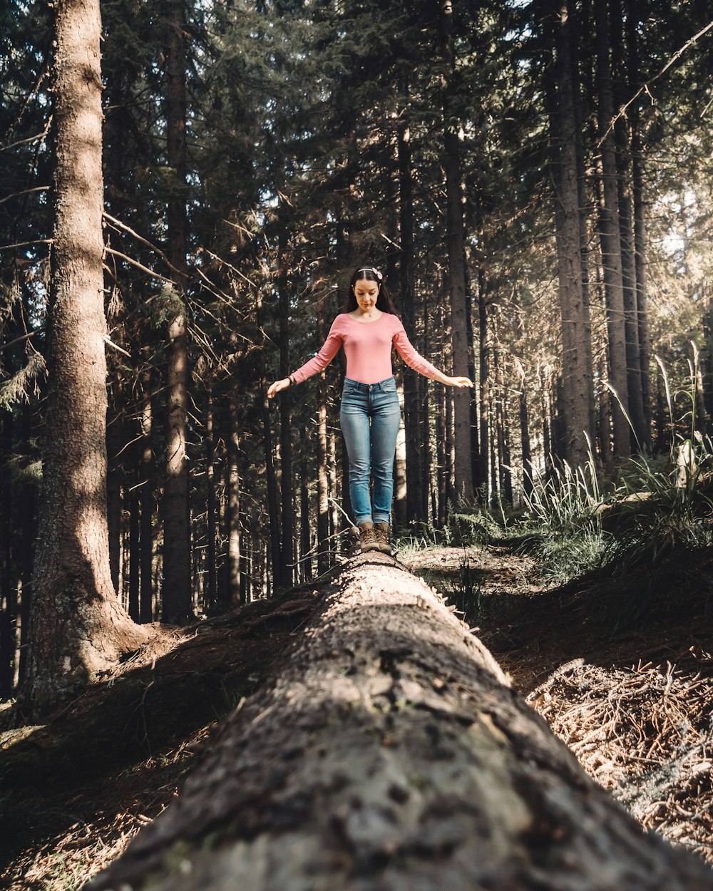 woman in blue denim jeans standing on brown tree log during daytime