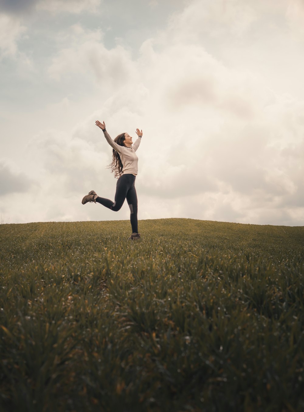 woman in white shirt and black pants jumping on green grass field during daytime