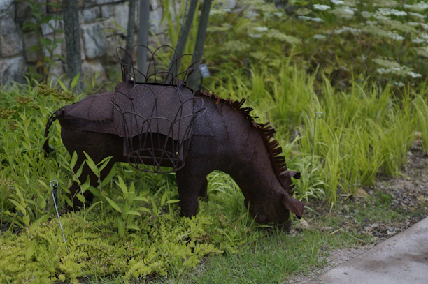 A close-up of a detailed metal animal sculpture nestled among garden plants.