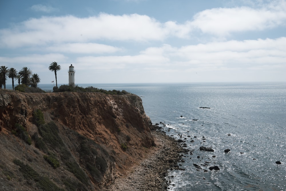 white lighthouse on brown cliff near body of water during daytime