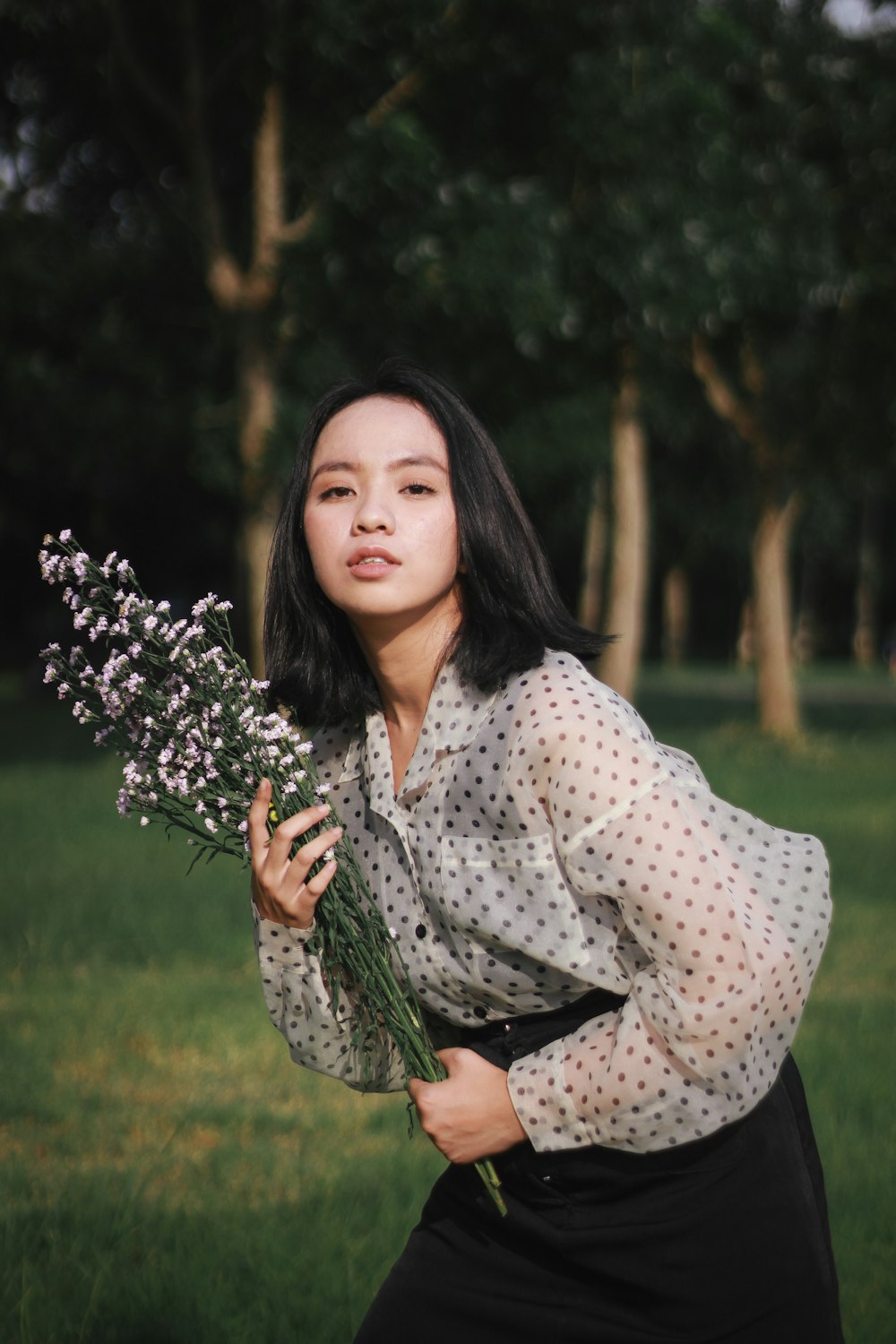 woman in white and black polka dot long sleeve shirt holding purple flowers