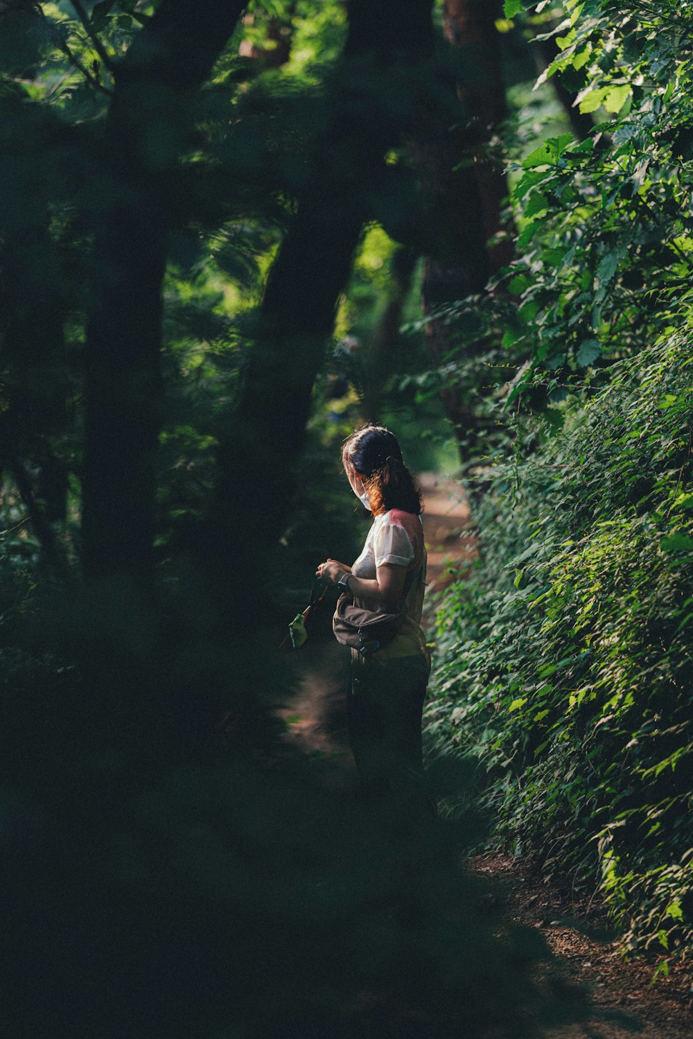 man in brown shirt and black pants carrying backpack standing in forest during daytime