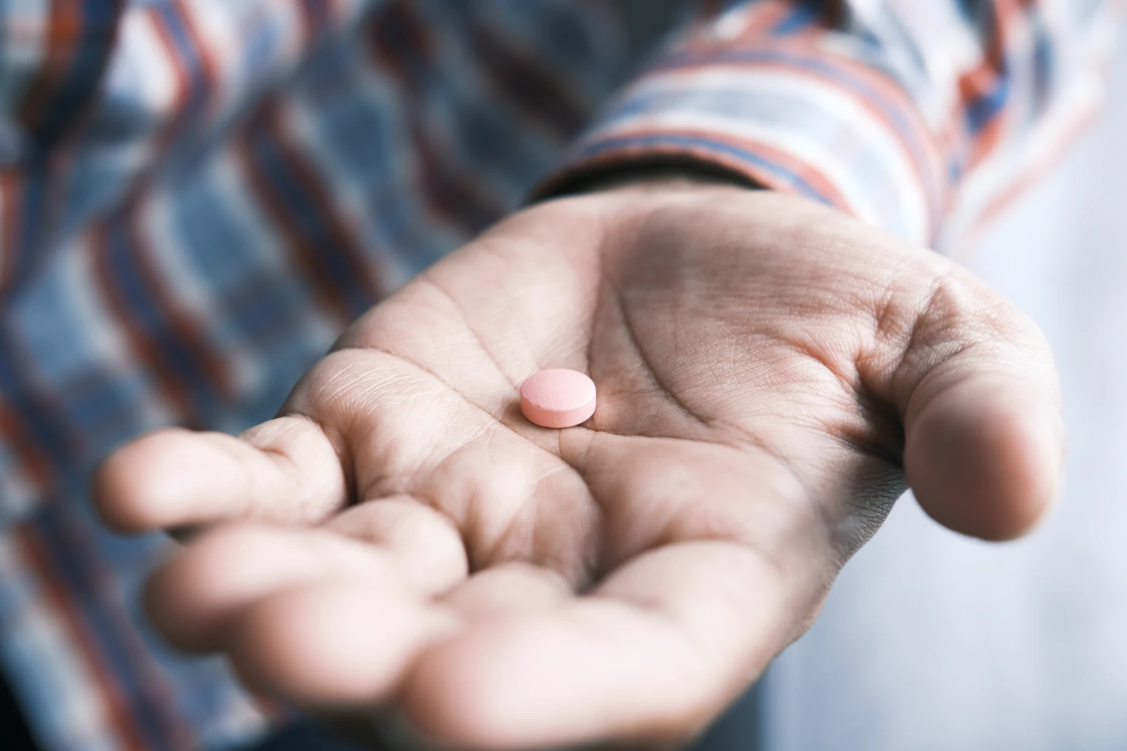 A hand offering a single medication tablet to another open hand — a moment of supportive care.