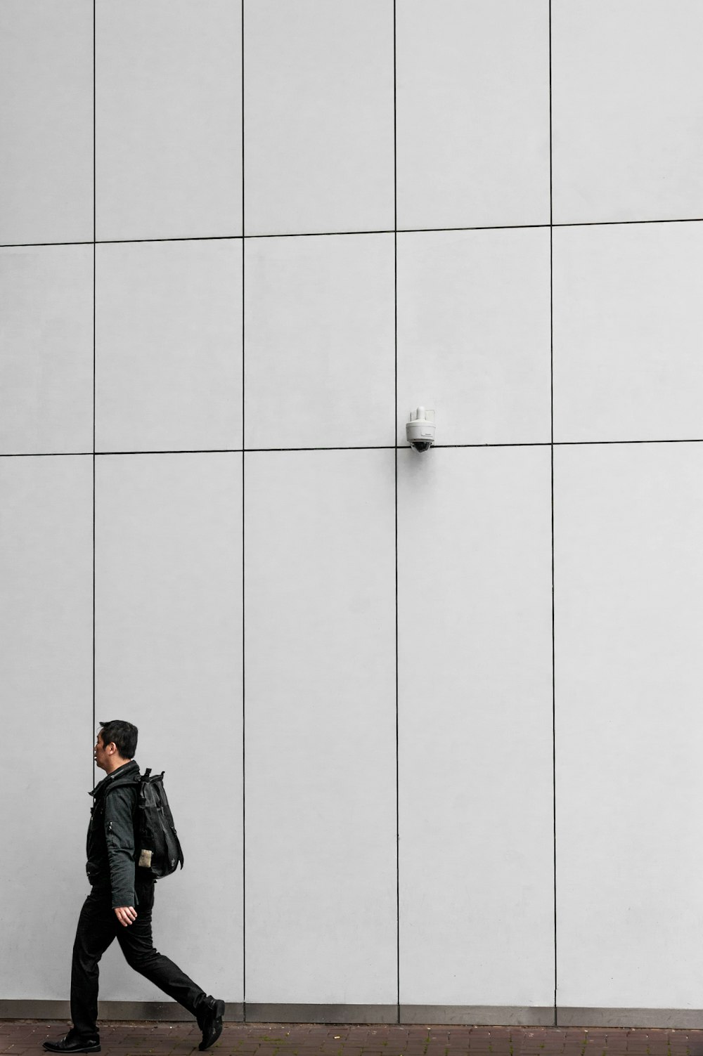 man in black jacket and black backpack standing beside white wall