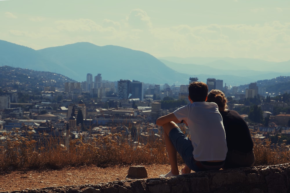 man and woman sitting on brown concrete fence during daytime